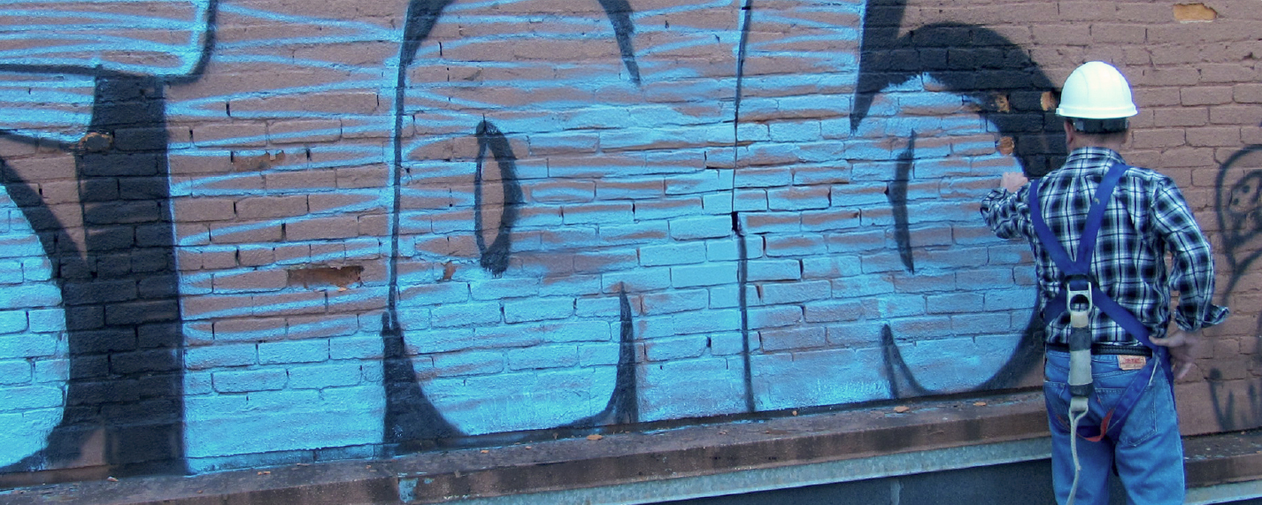 A man in a construction hat inspects a brick wall with graffiti art on it.